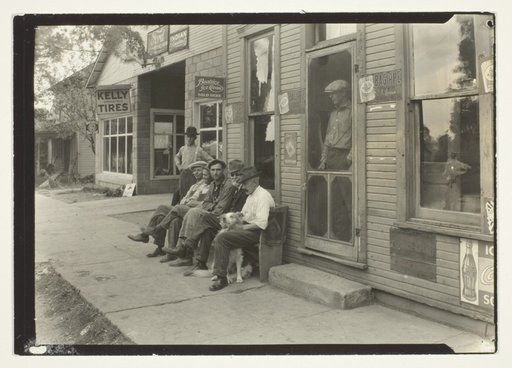 Men With Dog Sitting On Bench In Front Of General Store