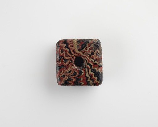 Black square with central hole decorated with white and red dragged wavy bands, possibly a weight