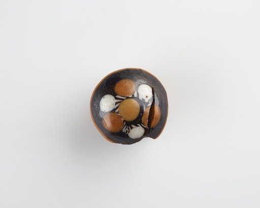 Black decorative knob with white and yellow inserts, originally applied to chest or cabinet