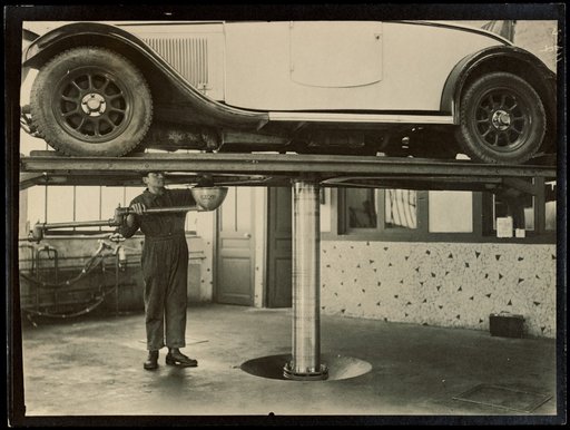 Auto Mechanic Standing Under Car Lift, Advertisement for "Desmarais"