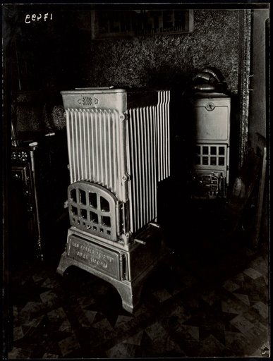 Several Metal Stoves with "SCHOLTÈS" Poster in Background, Advertisement for "Delmas"