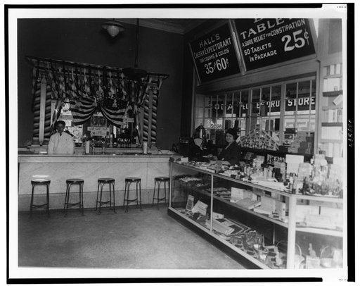 Interior of People's Drug Store, 14th and Park Streets, Washington, D.C., with employee behind soda fountain and another employee behind counter with product display