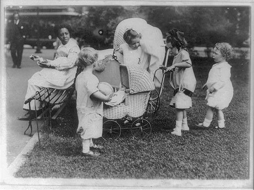 Four small children playing with baby carriages in Washington, D.C., park - African American nursemaid sitting on bench with baby