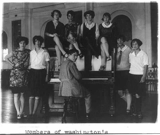 Man seated at piano, surrounded by group of glamourous girls, Washington, D.C.