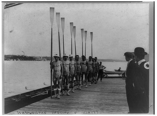 Washington Varsity 8 rowing team posed on dock holding oars
