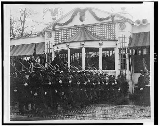 President Hoover and Mrs. Hoover standing in reviewing stand, watching soldiers march by during Hoover's inaugural parade