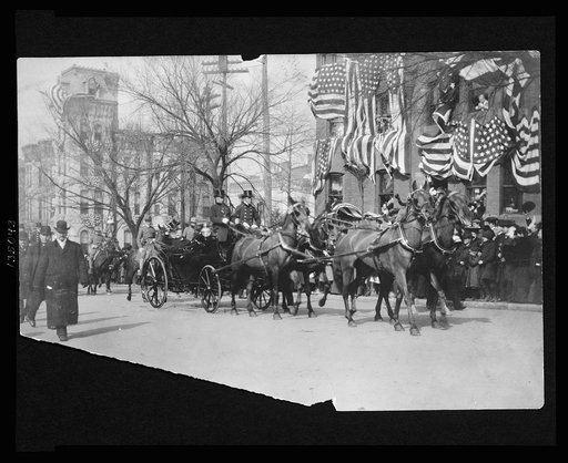 Theodore Roosevelt sitting in an open carriage enroute to the U.S. Capitol on his inauguration day tips his hat to spectators