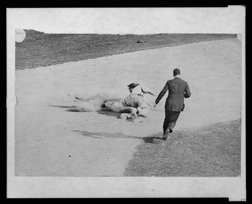 Umpire running to make call on man sliding into second base during baseball game