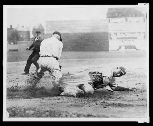 Umpire watches as New York Yankee player slides into base ahead of the tag during baseball game with Washington