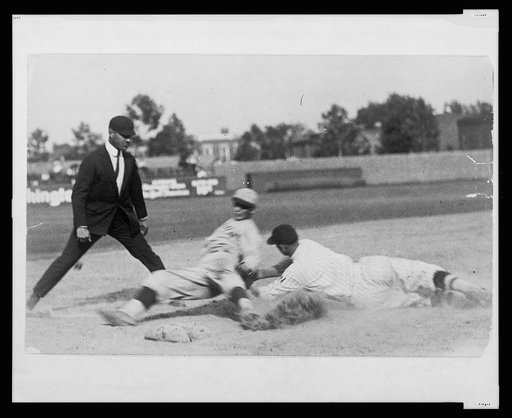 Umpire ready to make the call as Washington ball player applies tag to base runner sliding into base during baseball game