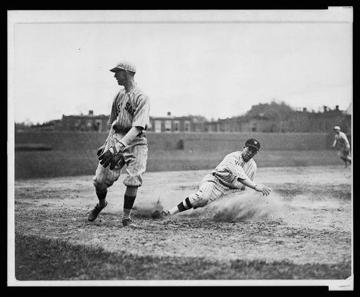 Washington Senators' Bucky Harris sliding, as he successfully steals third base in the 7th inning of a baseball game against the Boston Red Sox; third baseman Joe Dugan watches the ball roll toward left field after a wild throw. Senators shut-out Red Sox 10-0