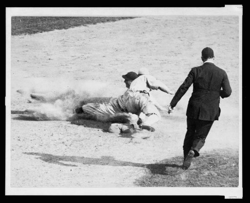 Umpire runs toward base to make the call on ball player sliding into second base during baseball game
