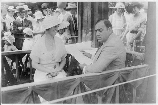 Enrico Caruso, 1873-1921, drawing caricature sketches in booth at charity fair in Southampton, L.I., with sitter, Mrs. Albert Gallatin