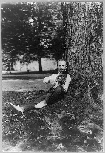 Mischa Elman, 1891-1967, sitting against tree, playing violin