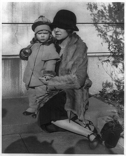 Alice (Roosevelt) Longworth, 1884- , full-length portrait, on her 43rd birthday, seated on step with her 2 year old daughter Paulyna, facing left