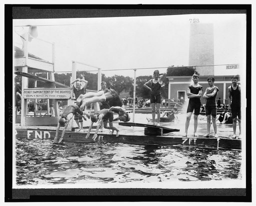 Boys diving, or waiting to dive, into a swimming pool