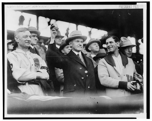 Calvin Coolidge, half length, standing, facing slightly right, holding up baseball at baseball game prior to opening game, 1925. L.to R.: Bill McKechnie, Coolidge, Bucky Harris
