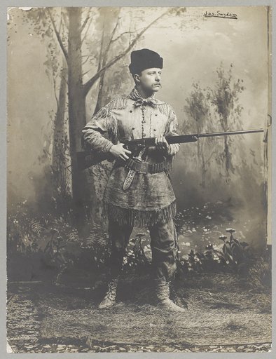 Theodore Roosevelt, full-length portrait, standing, facing right, in deer skin hunting suit, holding rifle