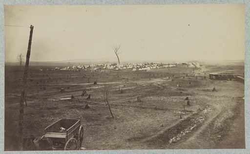 Wagon parked near a telegraph pole in foreground with a camp in the background