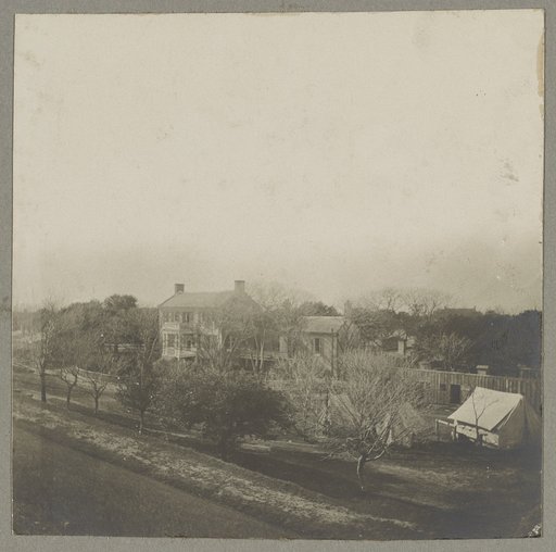 An aerial view of a house, tents, and other buildings partly obscured by trees