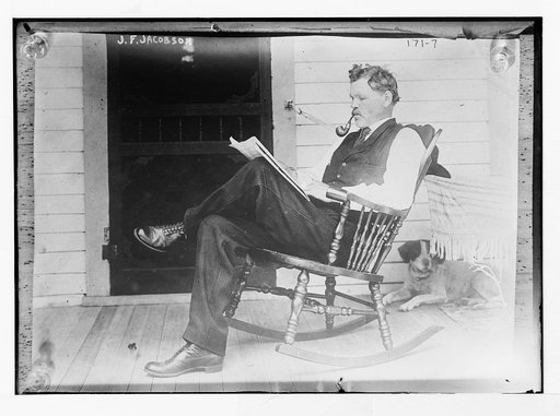 J.F. Jacobson, reading, in rocker, with dog