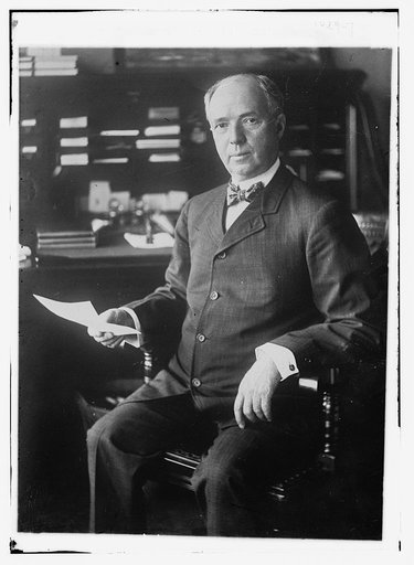 J.D. Archbold, seated holding paper