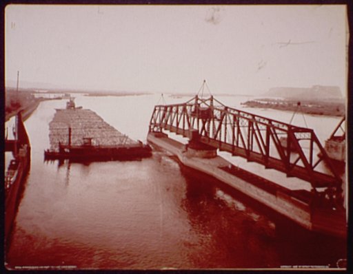 Winona, Minn., log raft passing draw bridge