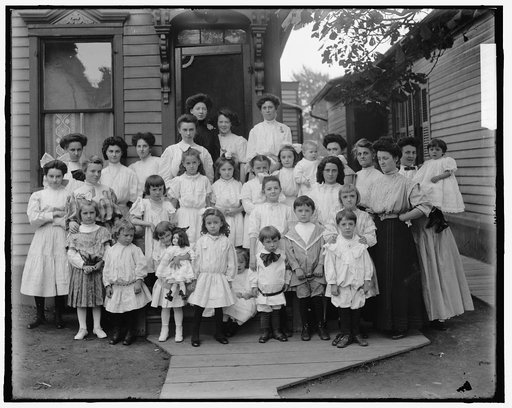 Children and women in front of house, possibly school children and teachers