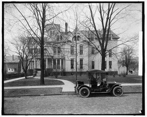 Three-story house with side porch and automobile in front, possibly Detroit, Michigan