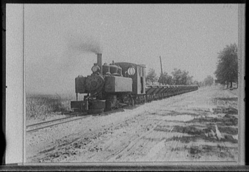 Locomotive pulling cars alongside road, possibly road construction in Michigan