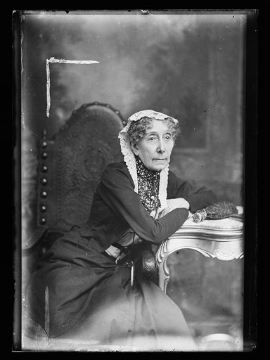 Elderly woman in lace cap leaning on table, three-quarter-length portrait