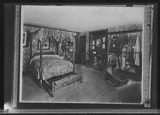 Bedroom with trundle bed, cradle, and costume display, possibly in historic house or museum