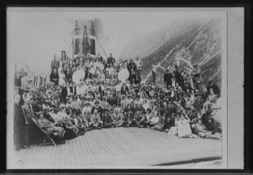 Passengers posed on deck of steamship in passage with steep cliff behind