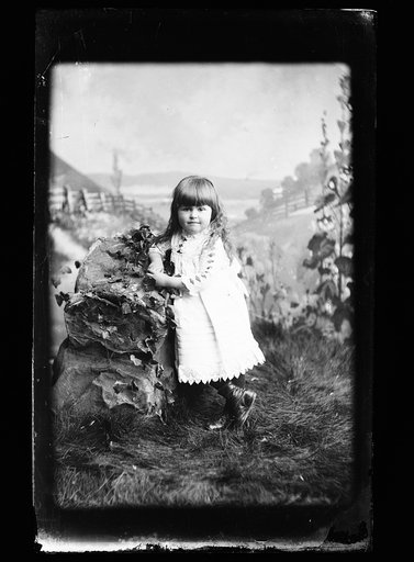 Girl, probably Hallie Jackson, in white dress posed against rock in studio background