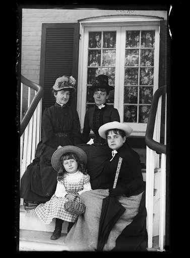 Three women and a girl in hats, seated on steps of house