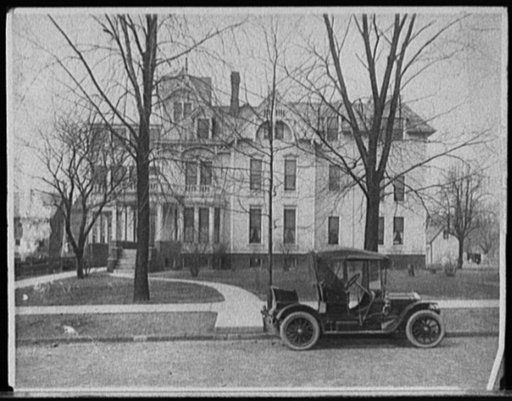 Three-story house with side porch and automobile in front, possibly Detroit, Mich.