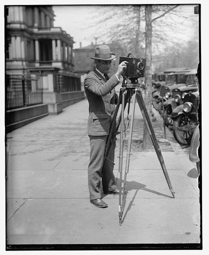 Man using a motion picture camera on a tripod, possibly a Debrie or Parvo "L" camera