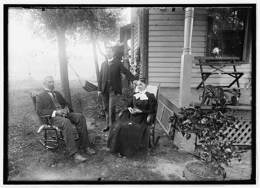 Unidentified men and woman seated in yard next to house