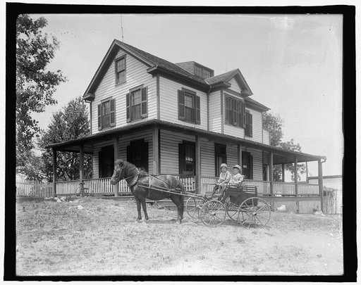 Children in horse-drawn wagon in front of house