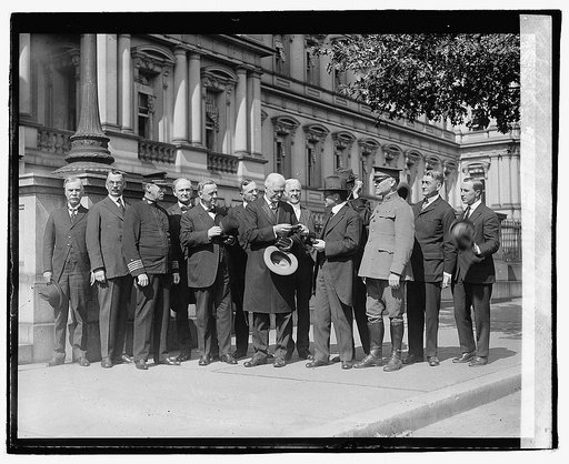 A group of men, including Daniels, Bishop McDowell and Baker, standing in front of the old State Dept. Building and passing around a little box, Oct. 4/20