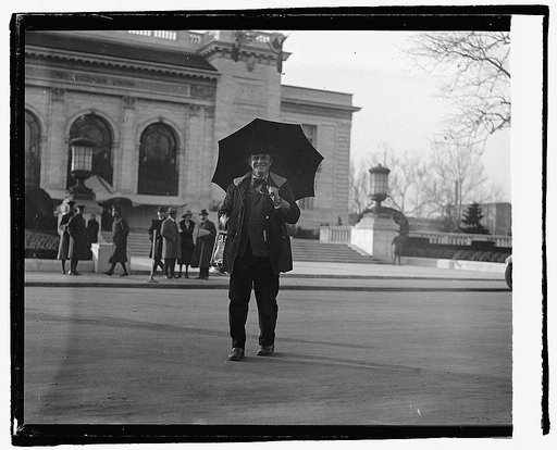 Unidentified man with umbrella standing in street with building in background], 12/15/21