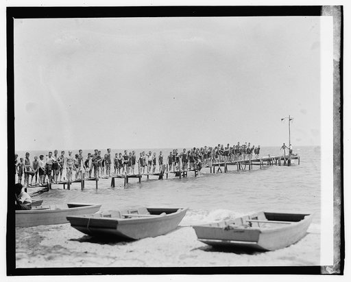 Group of boys standing on pier; beach with dinghys in foreground], 7/30/[23