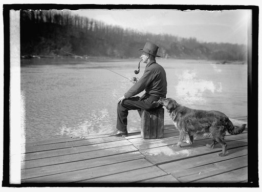 Hooch Hound, a dog trained to detect liquor (as suggested to Commissioner Haynes by a prohibition agent in Colorado), sniffs at flask in back pocket of man, seated, fishing on pier on the Potomac River