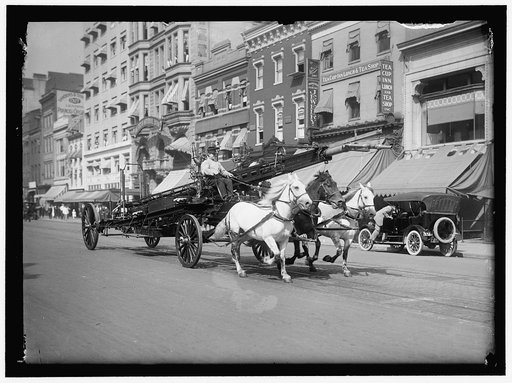 Three-horse team fire truck with water tower passing the 1300 block of F Street, N.W., Washington, D.C., with the Harris & Ewing studio in center above the driver's head, and the Sanders & Stayman piano store, 1327 F Street, at far left