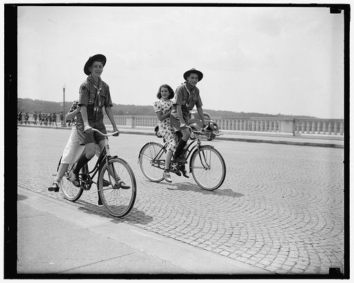 "On Bicycles Built For One." Washington D.C., June 30. The Boy Scout's motto of "do a good turn daily" was well observed by these Flint, Mich., scouts, John Kleinnheksel, and Dave Matthews, as they ride their girl friends across Arlington Memorial bridge despite the joshing of their comrades on the 