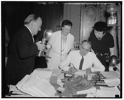 Speaker signs last minute bills. Washington D.C., Aug 21. Rep. John J. O'Connor New York, Chairman of the House Rules Committee, "shoots" Speaker Bankhead as he signs the last minute bills passed by the House before their adjournment tonight. Others in the picture are Rep. Mary T. [Norton] (left) of