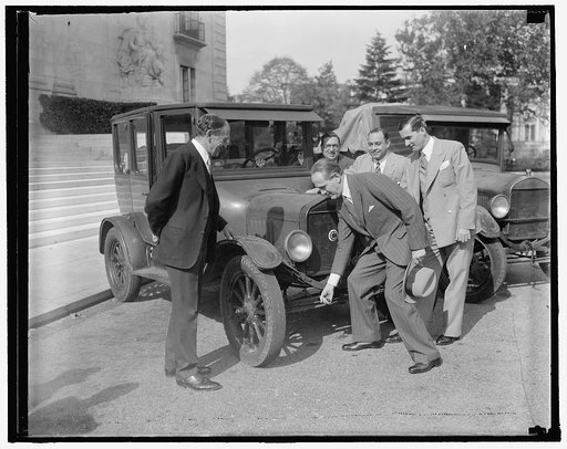 Brazilian Ambassador tries hand at cranking "Lizzie." Washington, D.C., Oct. 29. After hearing the experiences and hardships of the three Brazilian engineers, who finally arrived in the Capital today after a nine-year motor journey from Rio de Janeiro, Brazilian Ambassador Oswaldo Aranha tried his h
