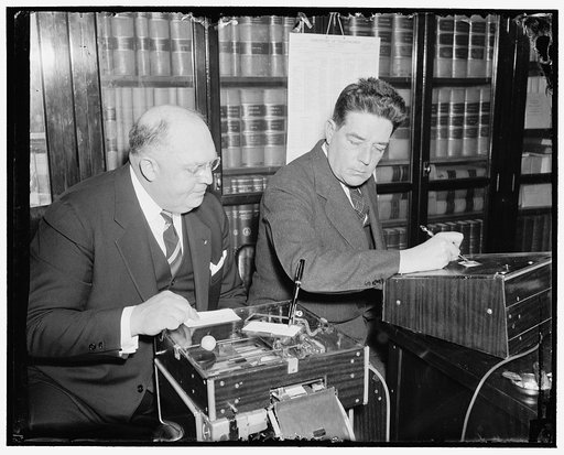 Demonstrates new signature machine to house member. Washington, D.C., March 18. The latest is the automatic electric signature machine invented by Glenn W. Watson, (left) who is shown in this picture demonstrating it to Rep. Lindsay C. Warren of North Carolina, 3/18/38