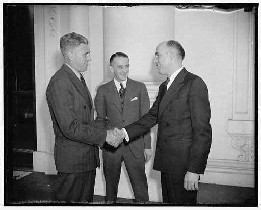 Incoming and outgoing. Washington, D.C., April 14. Today marked the change in chief ushers at the White House. Raymon Muir, who resigned as chief usher today to become assistant to the Chief of International Division of the State Department, is bid goodbye by Howell Crim, his successor. In the cente