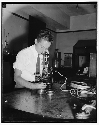 Government discovers method to preserve film. Scratch resistance, film, particulary the emulsion side, may become damaged through scratching. D. Levinsky of the Bureau is using an instrument which tests the resitance of a film by measuring the width of a scratch produced by a diamond point under a g